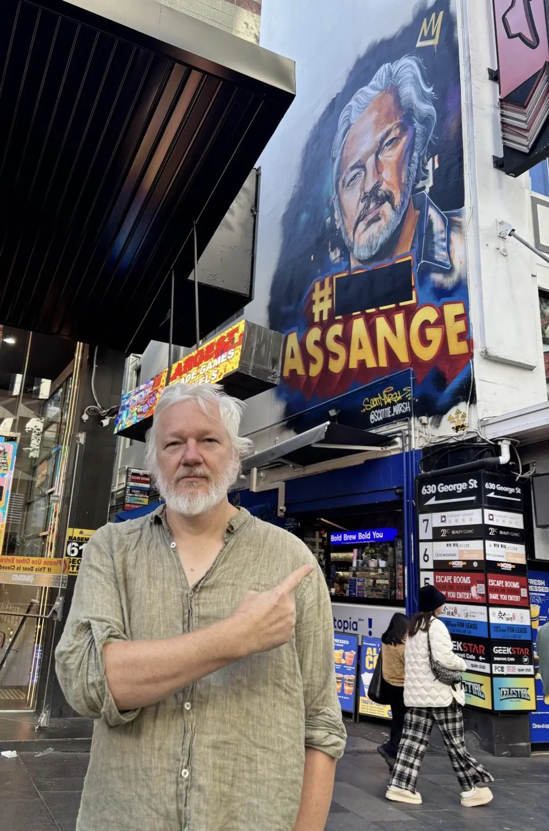 جولین آسانژ (Julian Assange) در کنار نقاشی دیواری بزرگ از چهره خود در خیابان